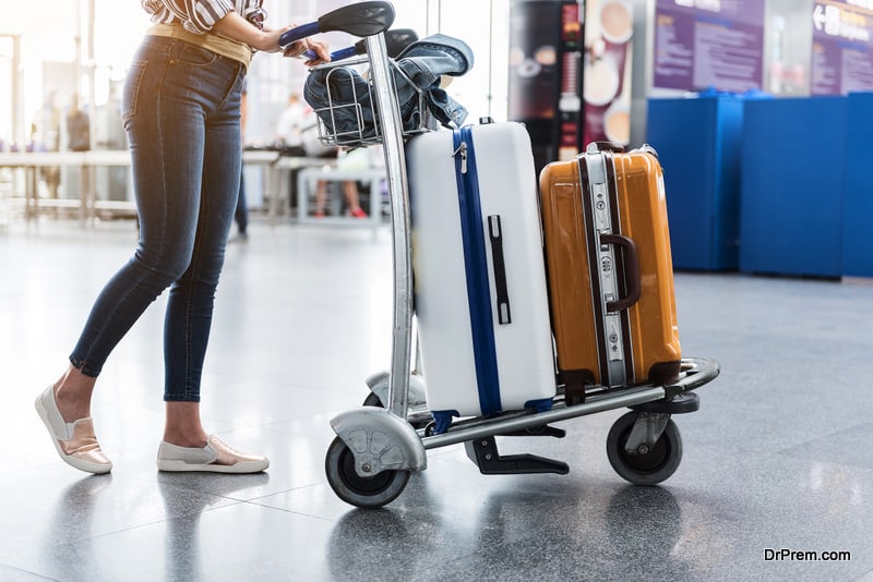 Female person is walking through airport-foyer with her luggage at small cart. Focus on baggage. Close up of her legs