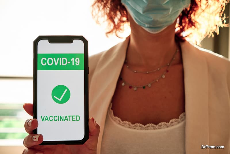 a woman with protective mask showing covid-19 vaccination certificate on smartphone