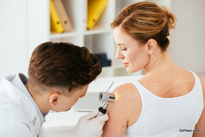 Dermatologist in latex gloves holding dermatoscope while examining attractive patient with skin disease