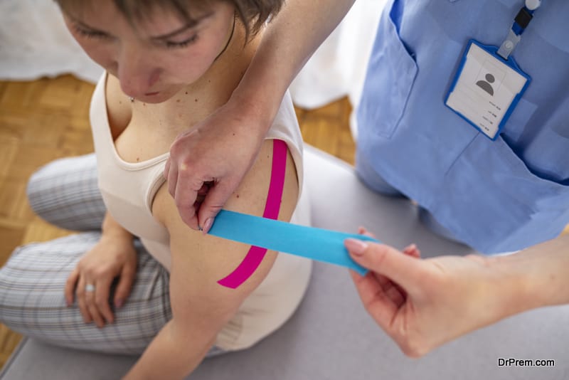 Female physiotherapist applying tape on a female patient. Shoulder treatment with kinesio tape