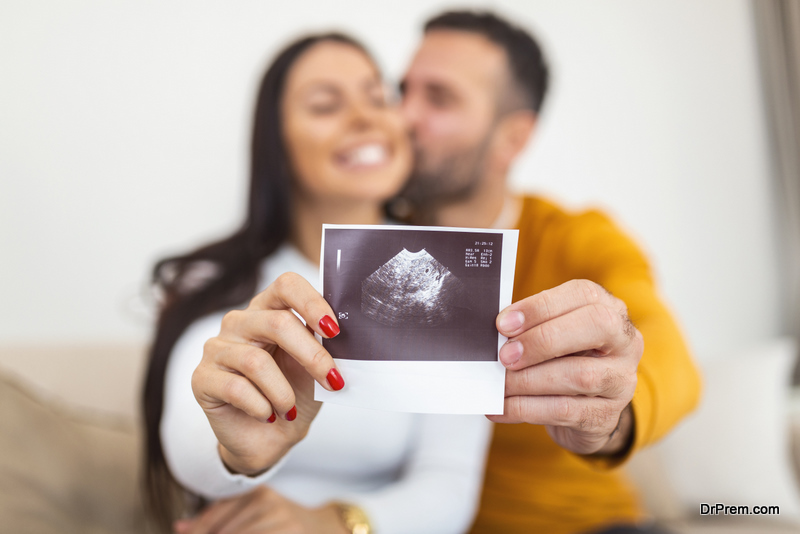 Happy pregnant woman with baby ultrasound photo embracing with her husband