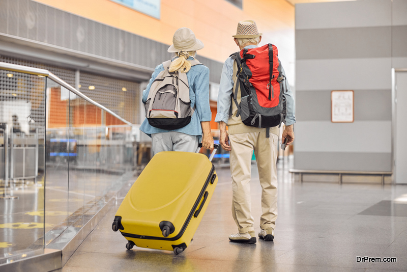 Back view of a senior lady with a trolley suitcase and a man with a boarding pass