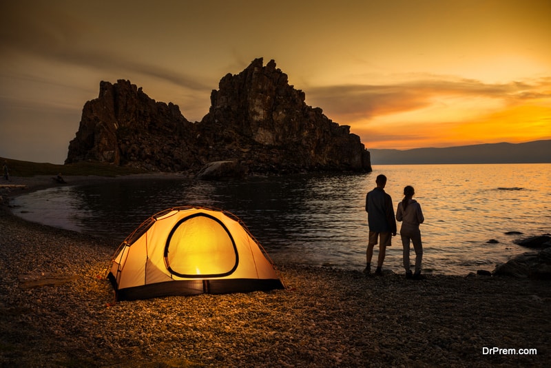 Couple stand at tent and Baikal lake shore and looking at the sunset