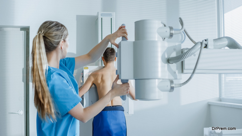 In the Hospital, Man Standing Face Against the Wall While Medical Technician Adjusts X-Ray Machine For Scanning.