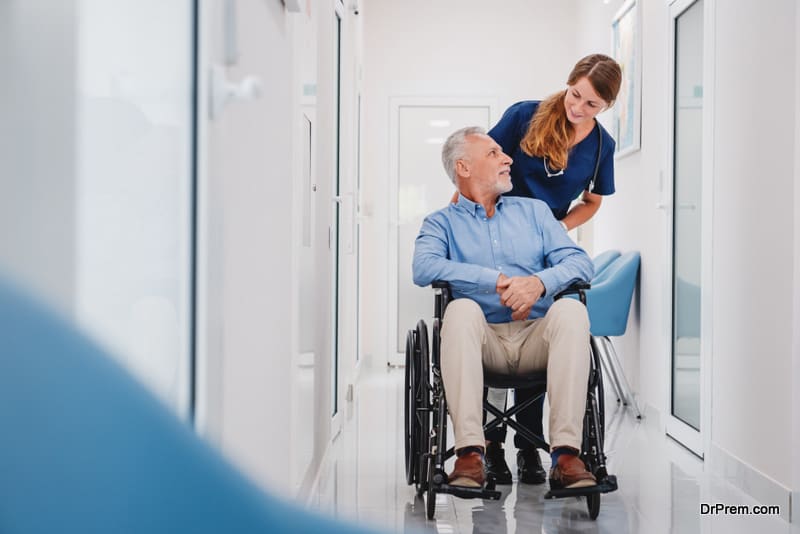 Senior male patient sitting in wheelchair in hospital corridor with female nurse doctor