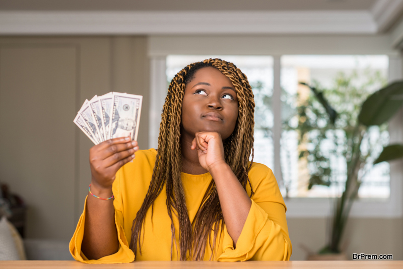African american woman holding dollars serious face thinking about question, very confused