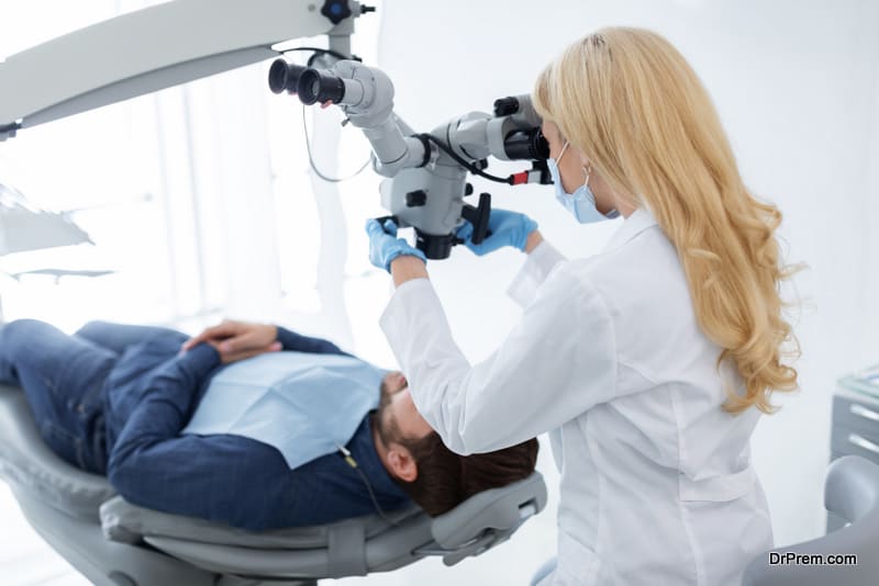 Female stomatologist making treatment for male patient, using dental microscope