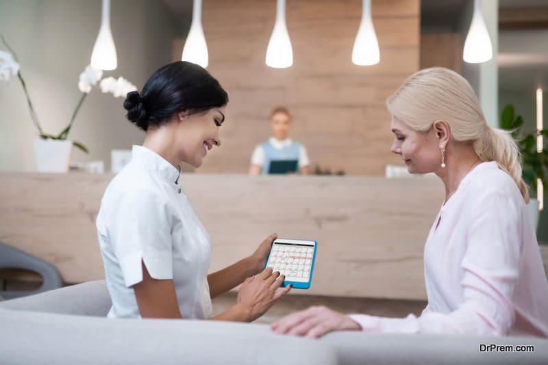 Planning together. Smiling woman sitting on the sofa with her dentist holding a tablet with calendar fixing a meeting.