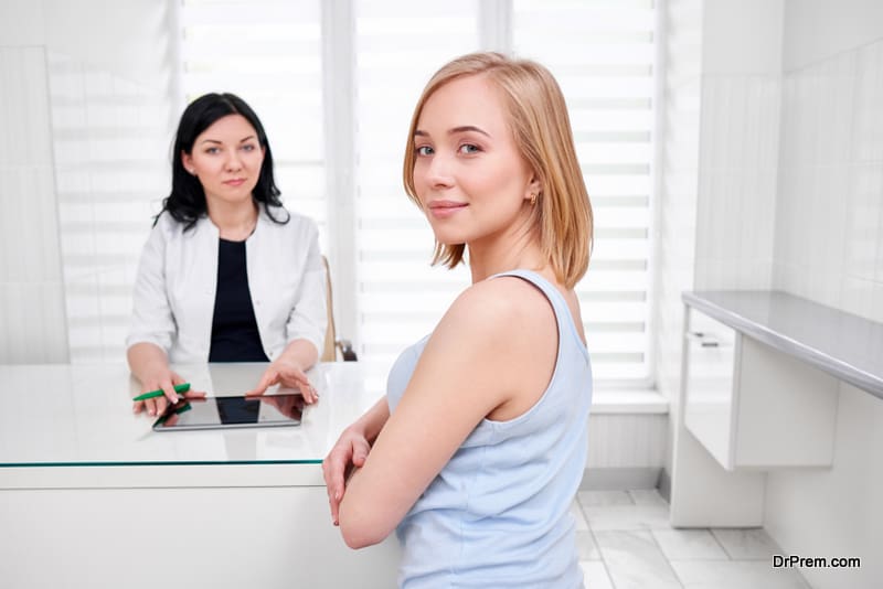 Beautiful young woman smiling to the camera over her shoulder while visiting doctor at the hospital