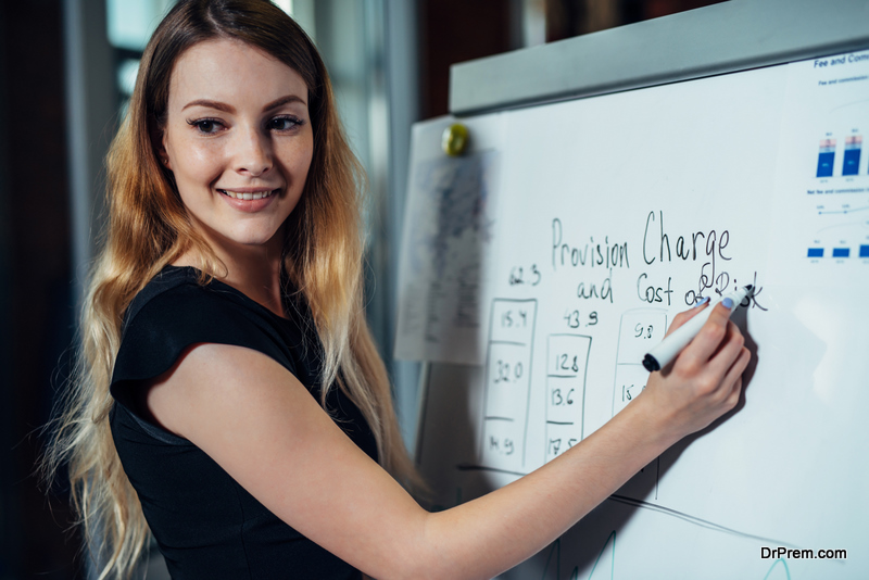 Portrait of young female leader writing on whiteboard explaining new strategies during the conference in an office.