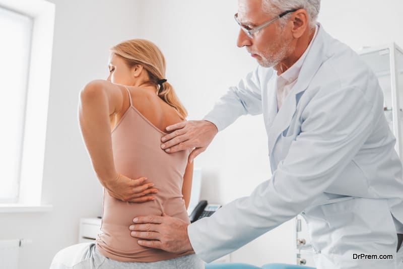 Senior male orthopedist examining patient's back in clinic