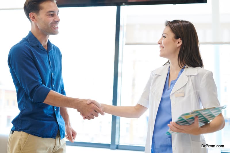 Waist up portrait of young female doctor shaking hands with happy patient after successful treatment in modern clinic