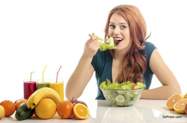 Happy woman having a table full of organic food,juices and smoothie. Cheerful young woman eating healthy salad and fruits. Isolated on white.