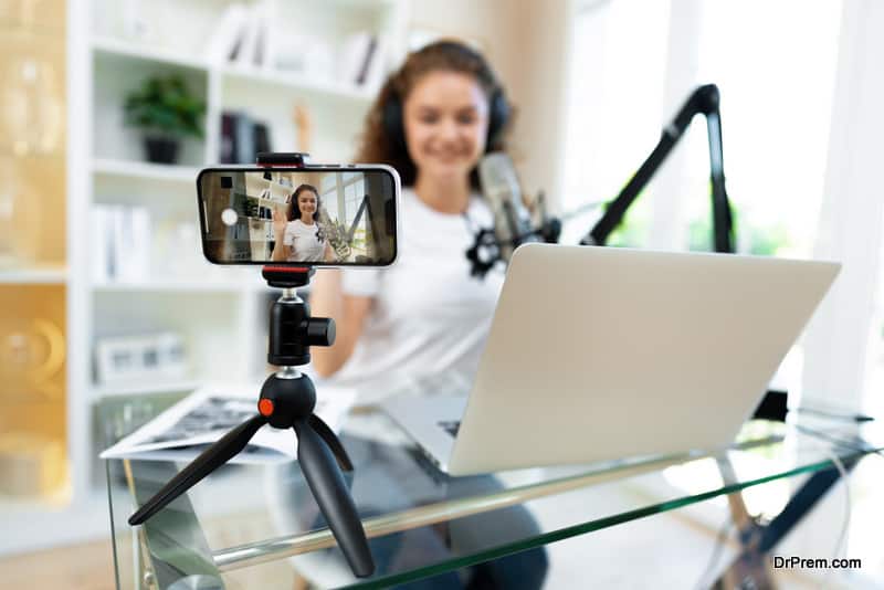 young-curly-female-blogger-recording-video-at-table-at-home