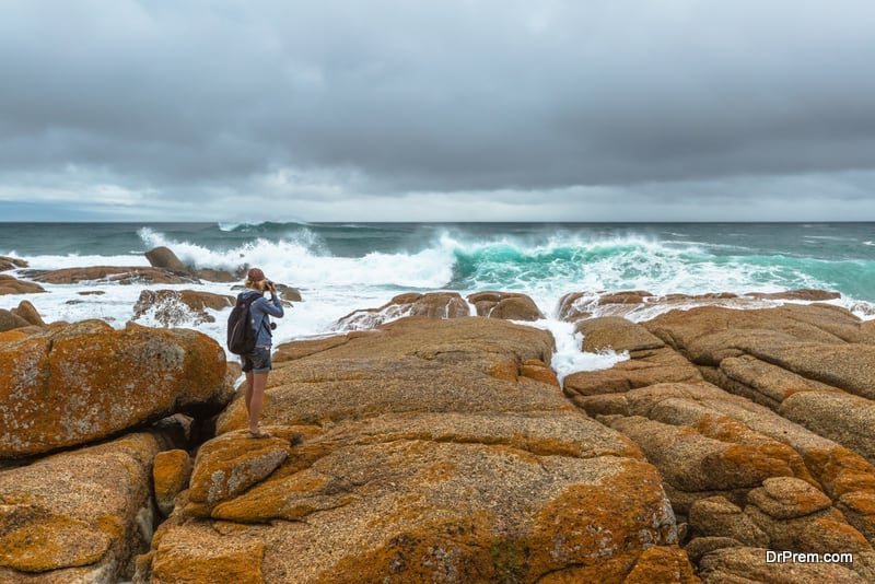 Nature travel photographer woman taking pictures on a cliff in Redbill, famous beach for wind, waves and suf. Tasmania, Australia