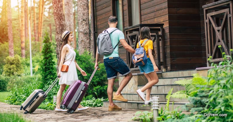 glad family with suitcases and backpacs on a weekend coming to the hotel surrounded by trees