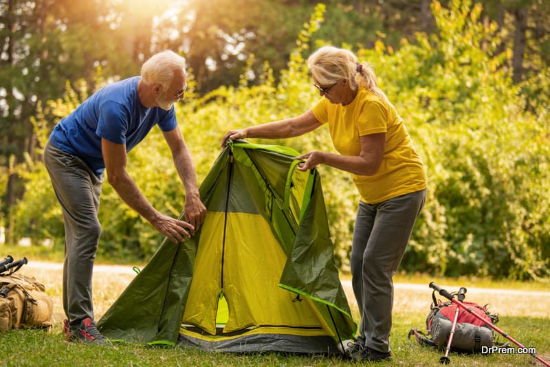 Senior couple spreading the tent in the forest after hiking