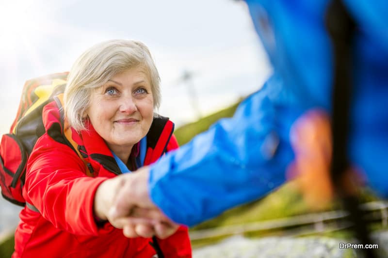 Senior tourist couple hiking, man is helping woman to get to the rock