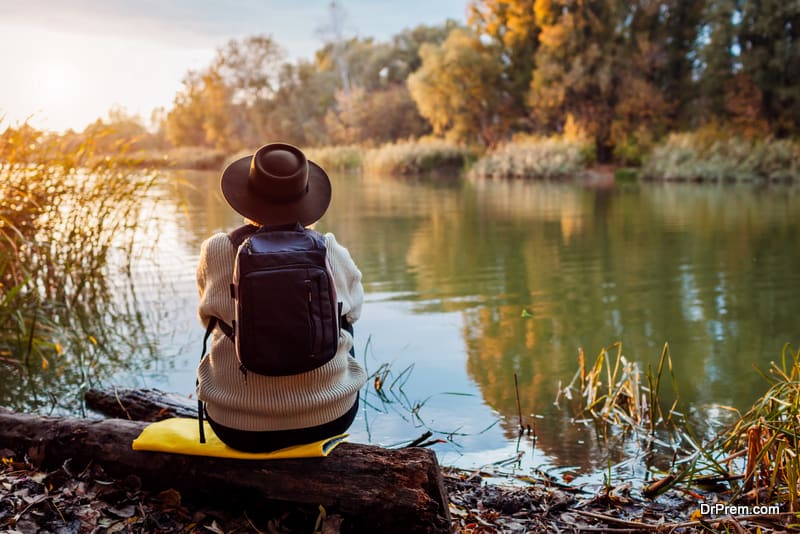 Tourist with backpack sitting on river bank at sunset