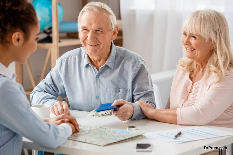 Travel agent at office sitting with senior clients man givving passport and money