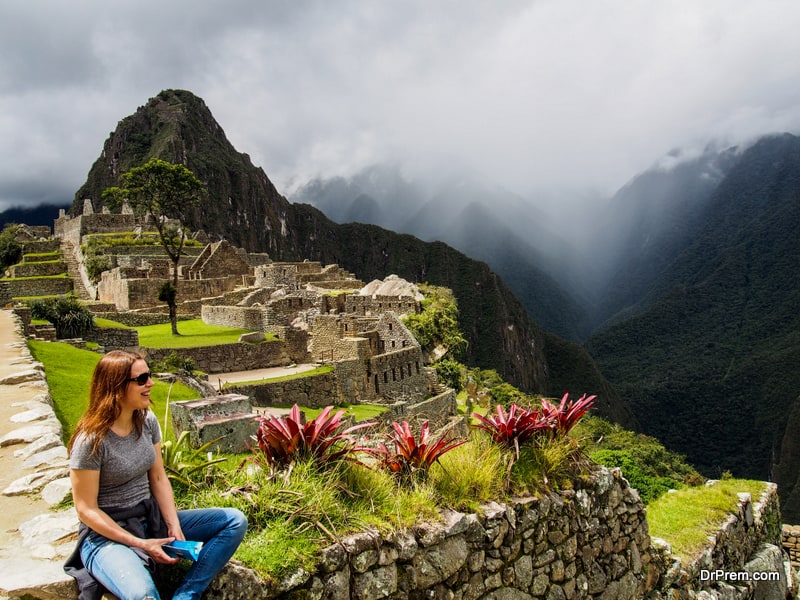 Cheerful-Woman-Sitting-at-Ancient-Stone-and-Looking-at-Machu-Picchu-Mountains