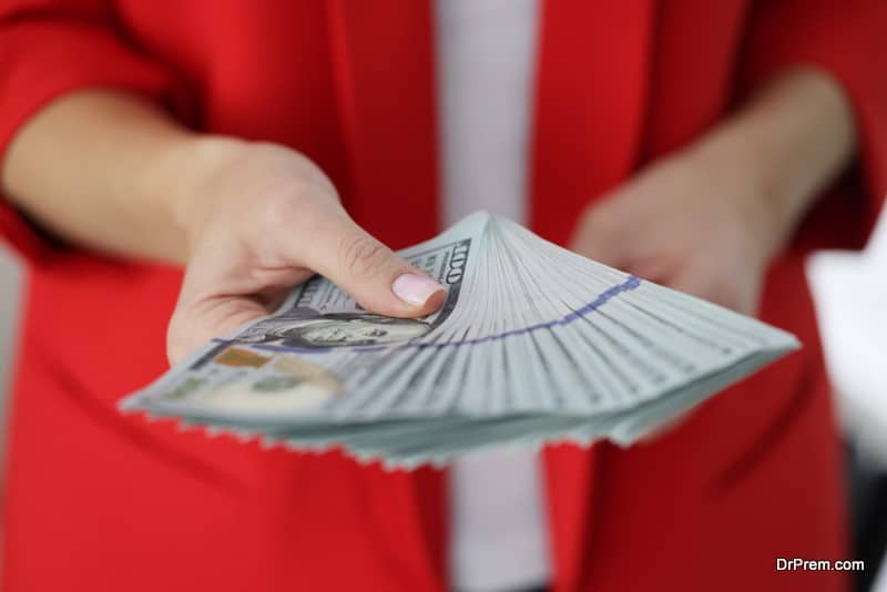 Woman in red jacket holding lot of American dollar bills in hands