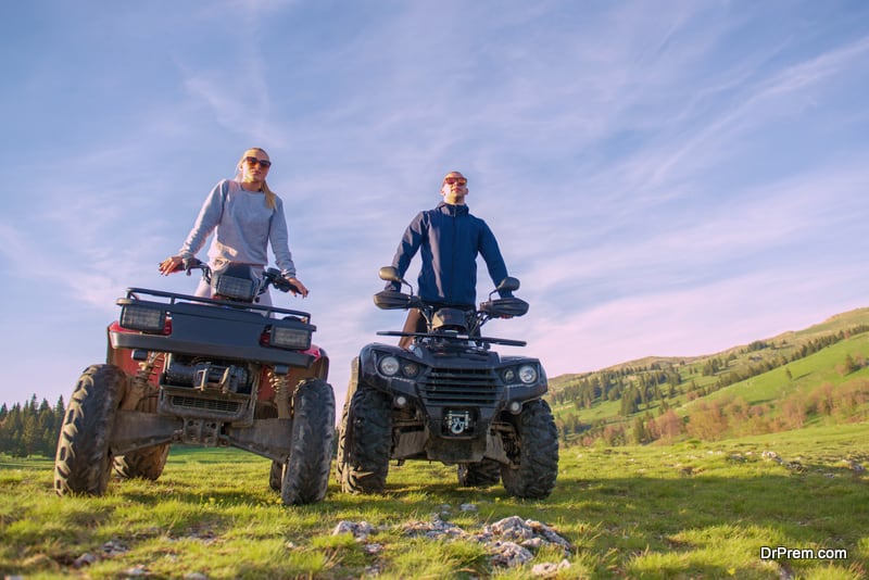 Beautiful couple is watching the sunset from the mountain sitting on atv quadbike