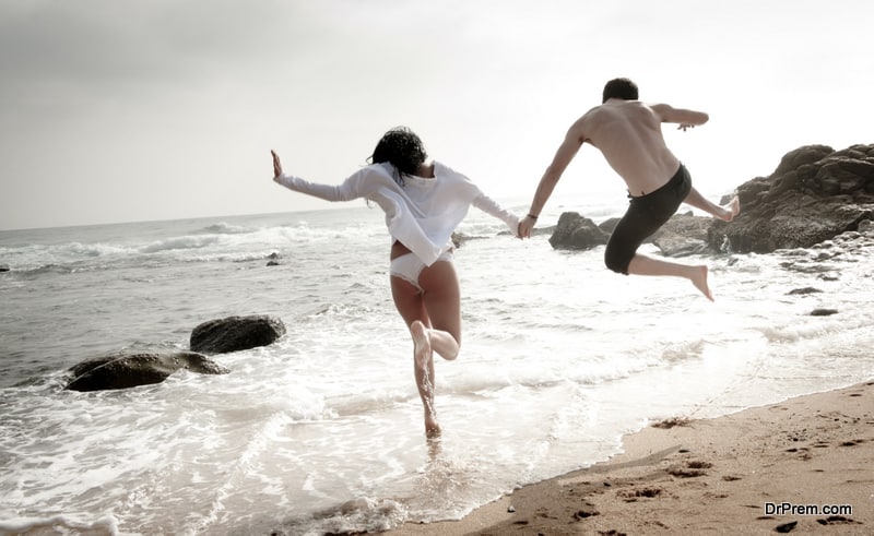 Young caucasian couple jumping into the water at beach