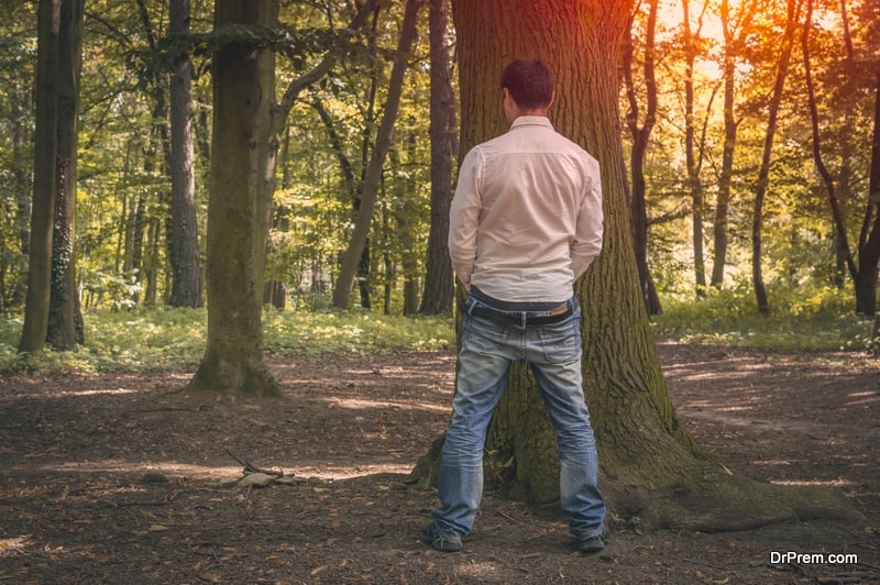 Standing man peeing near big tree