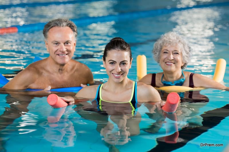 Happy mature man and old woman doing aqua aerobics with foam rollers in swimming pool