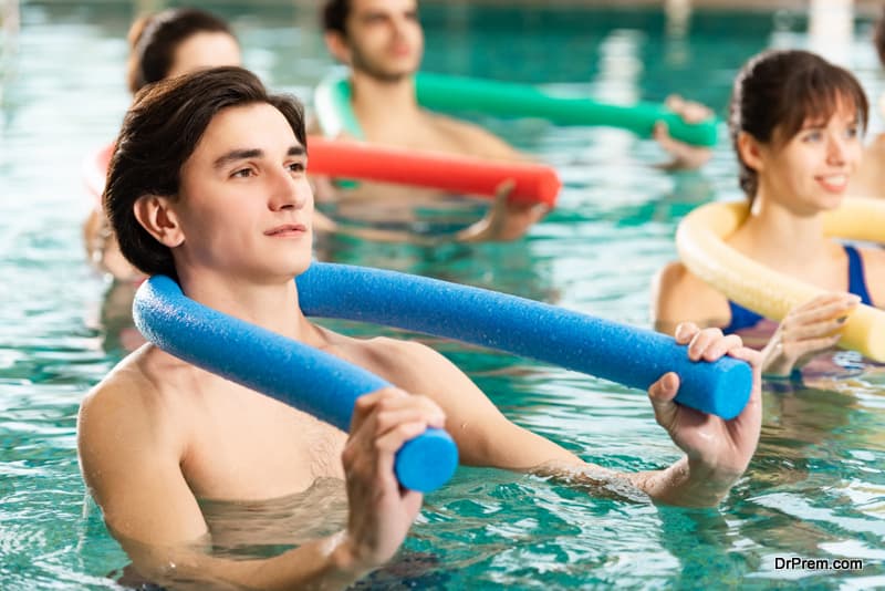 Selective focus of young man holding pool noodle during exercise in swimming pool