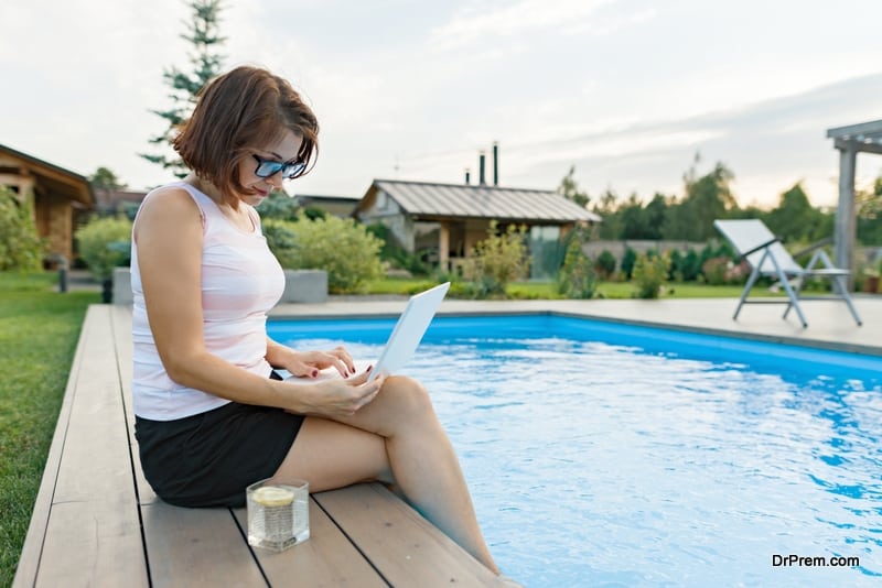 Mature woman with laptop near private home pool, successful beautiful female freelancer.