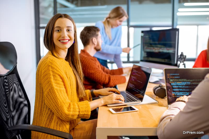 Team of a young woman as a programmer sitting in the office with people working on the background