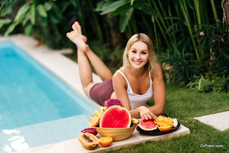 Woman relaxing and eating fruits in the pool on luxury villa in Bali. Exotic summer diet. Tropical beach lifestyle.