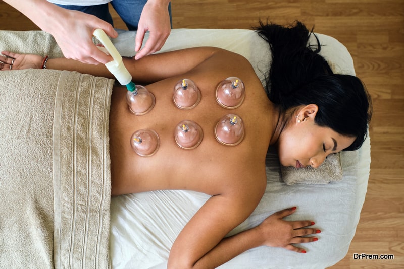 Adult masseuse giving cupping massage to young ecuadorian girl lying on the spa table with her eyes closed. Horizontal and high angle photography.