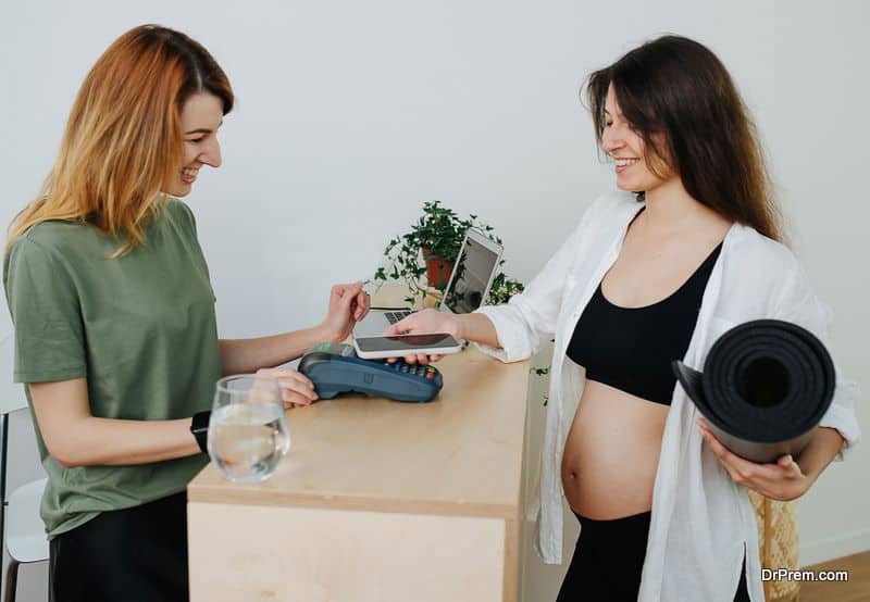 Cheerful pregnant young woman paying for her yoga practice