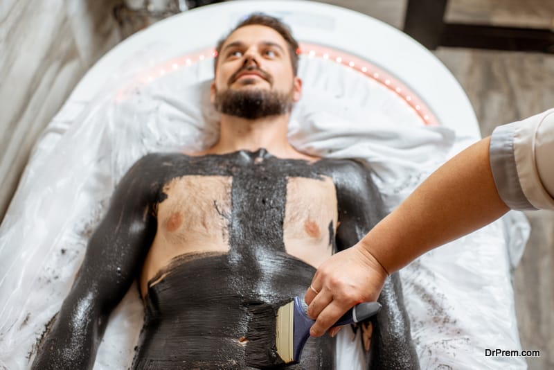 Man during a mud wrapping with special black mud, lying in the spa salon. Concept of a Detox mud body wraps
