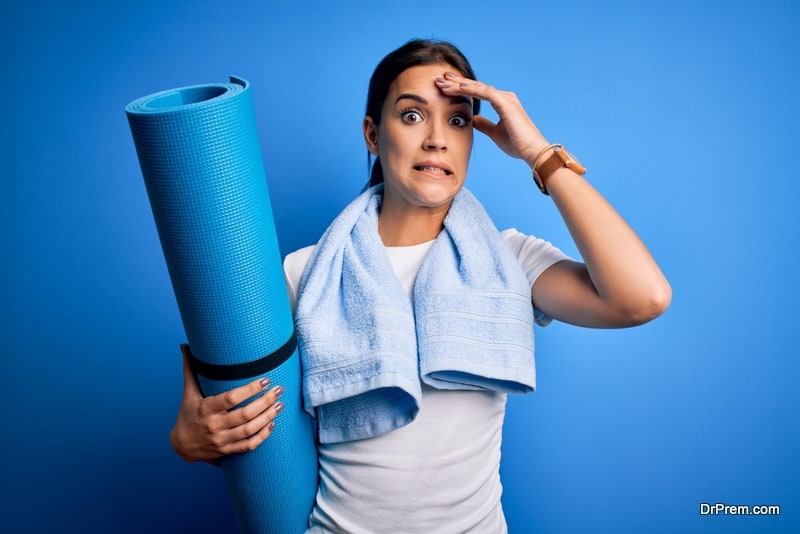 Young beautiful brunette sportswoman wearing towel holding mat to do yoga stressed with hand on head