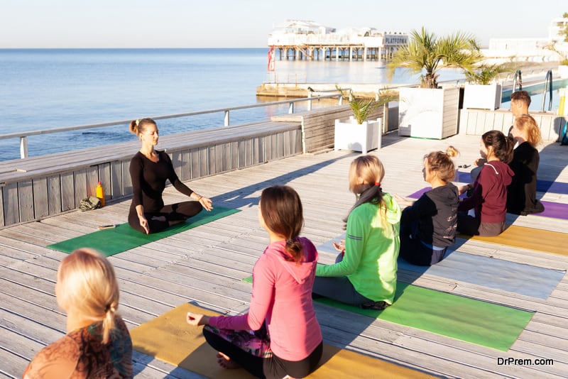  group of women meditating in lotus pose outdoor on wooden terrace. 