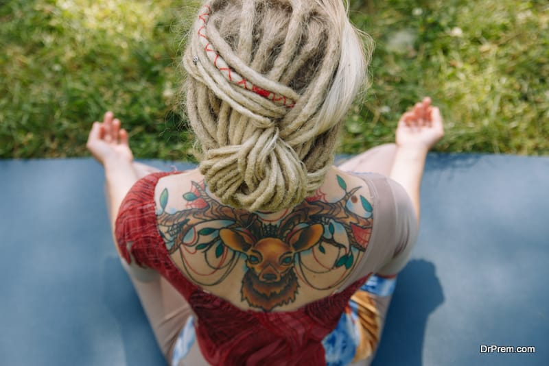 rear view of woman practicing yoga in lotus pose in the forest (Park) with green leaves