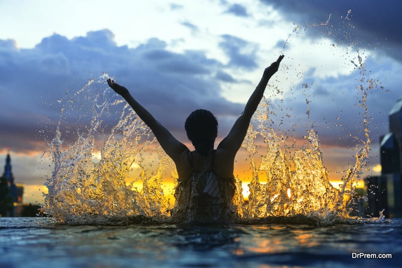 Black silhouette of asian woman splash water on summer vacation holiday relaxing in infinity swimming pool 