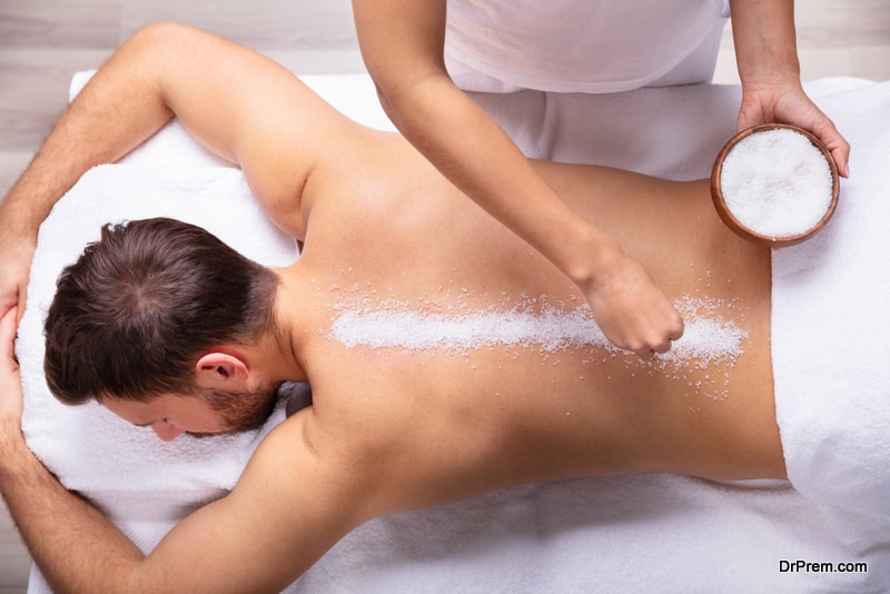 Close-up Of Therapist Hand Applying Salt On Young Man's Back