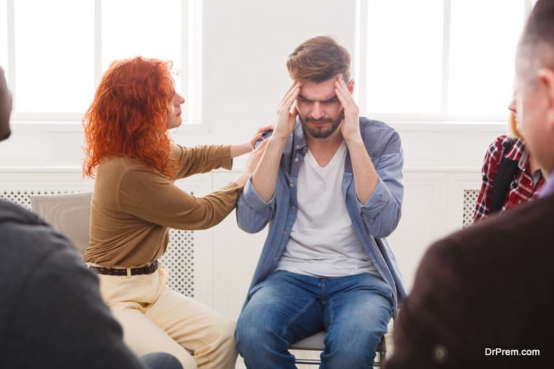  Young depressed man with headache sitting at rehab group therapy. 