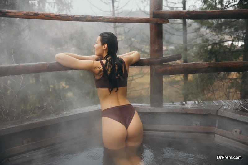 Young woman in a bikini bathing in wooden bath outdoors while raining. 
