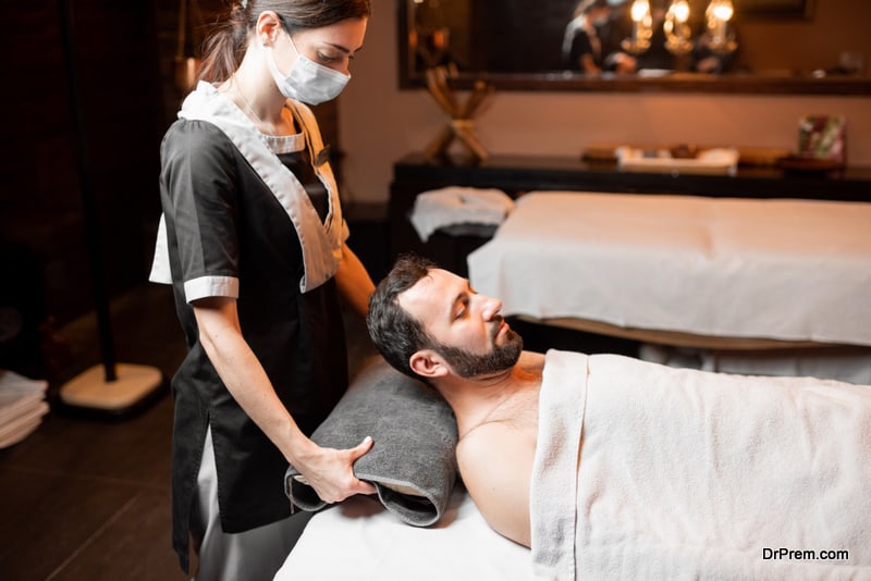 Professional female masseur in medical mask doing facial massage to a male client at Spa salon. Business during the epidemic concept