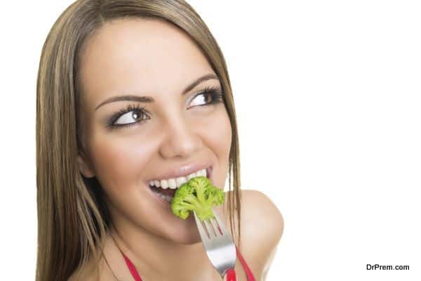 Happy young woman eating broccoli