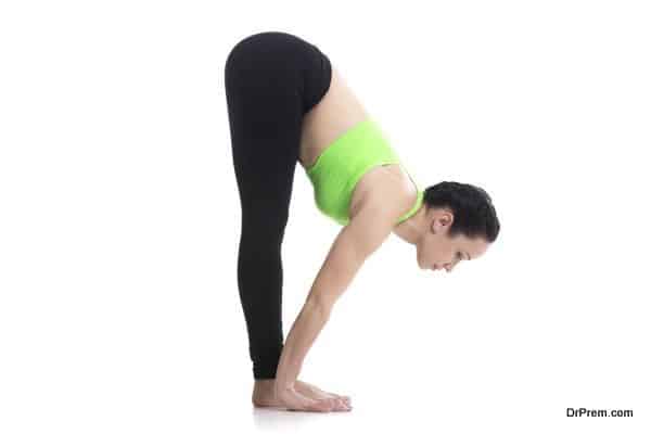 Sporty girl on white background in standing forward bend yoga pose (uttanasana), asana from surya namaskar sequence, sun salutation complex, posture for leg muscles