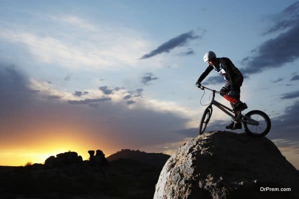 Bike rider balancing on rock boulder, side view