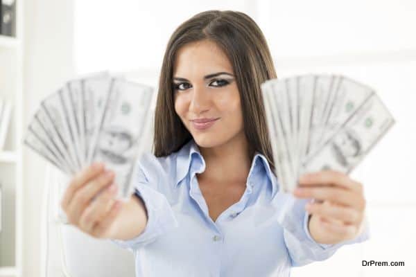 Young pretty woman holding money in her hands outstretched, with a slight smile looking at the camera, the money is out of focus.