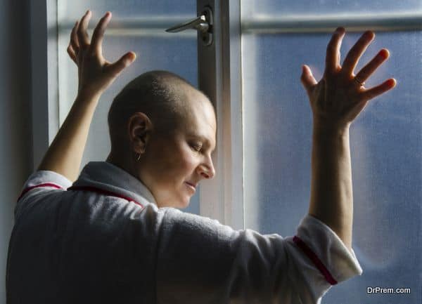 Bald woman suffering from cancer leaning on the hospital window